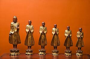 Wooden statues of Buddha with five disciples against orange wall.