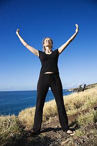 Caucasian mid-adult woman standing on Maui, Hawaii coast with arms outstretched and eyes closed.