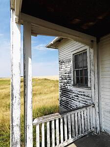 View from porch of weathered abandoned building in grassland.