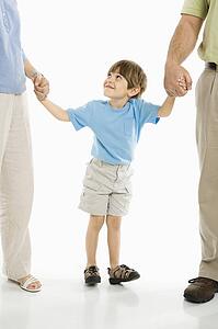 Boy holding hands with parents standing against white background.