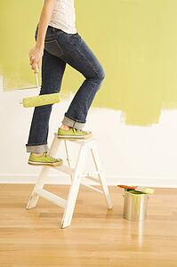 Legs of woman climbing stepladder holding paint roller