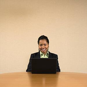 Businesswoman sitting at conference table smiling and typing on laptop computer.