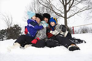 Portrait of happy Caucasian family of four sitting in snow smiling at veiwer.