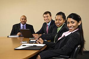 Businesspeople sitting at conference table smiling.
