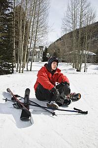 Caucasian male teenager sitting on snow with ski gear.