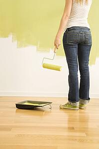Back view of woman holding paint roller with half painted wall 