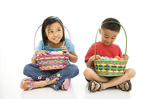 Girl and boy sitting on floor holding Easter baskets full of eggs