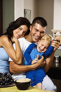 Family with toddler son in kitchen at breakfast smiling