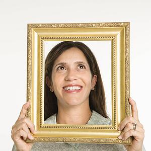 Woman holding frame in front of face smiling.