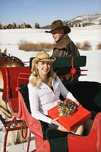 Woman holding a present while man drives horse-drawn sleigh