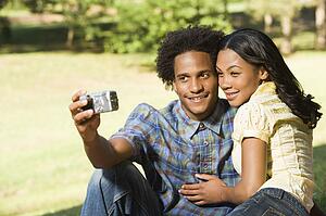 Happy smiling couple taking pictures together in park with digital camera.