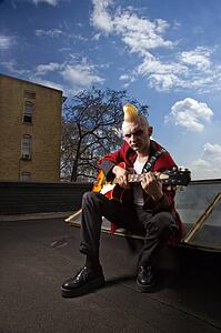 Portrait of a mid-adult male punk sitting on a skylight playing guitar