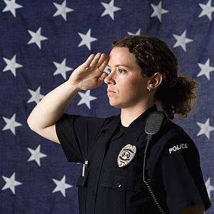 Portrait of mid adult Caucasian policewoman saluting with American flag as backdrop.