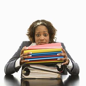 Businesswoman resting head on large stack of books and files looking overwhelmed