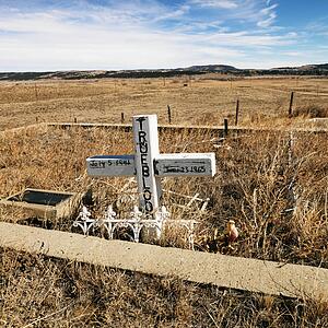 A cross tombstone in cemetery with landscape in background.