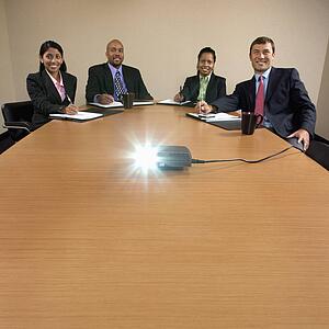 Businesspeople sitting at conference table watching LCD projector presentation.
