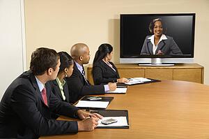 Businesspeople sitting at conference table looking at flat screen display