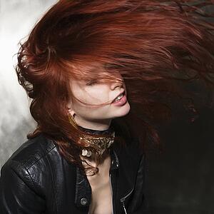 Caucasian woman in leather jacket tossing long hair in air. 
