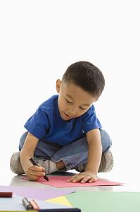 Asian boy sitting on floor coloring on paper.