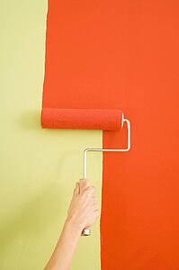 Female hand painting with red onto a green wall