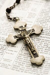 Crucifix on rosary lying on open Bible