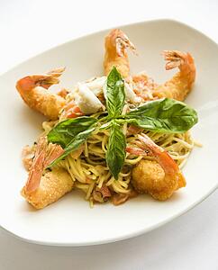 Gourmet meal with fried shrimp and pasta garnished with fresh basil.