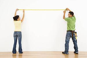 Couple measuring interior wall and smiling