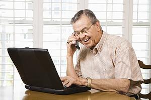 Man typing on laptop and talking on cellphone