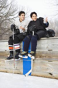 Boys in ice hockey uniforms sitting on ice rink sidelines pointing and looking