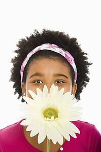 Girl holding large Gerbera Daisy over face and looking at camera