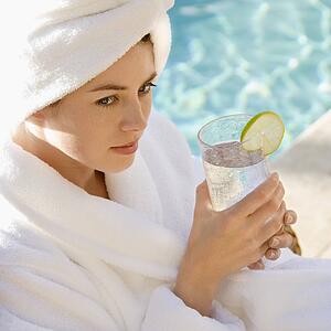 Woman wearing robe and towel on head drinking from glass next to pool