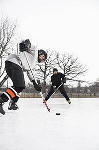 Two boys in ice hockey uniforms skating on ice rink moving puck.