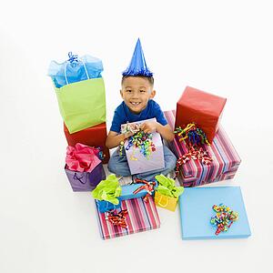 Asian boy wearing party hat sitting with pile of wrapped presents.