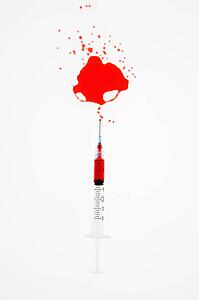 Hypodermic needle with red liquid sprayed on white background.