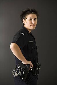 Portrait of mid adult Caucasian policewoman standing with hand on gun holster looking at viewer.