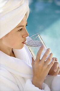 Woman wearing white terry robe drinking water next to pool