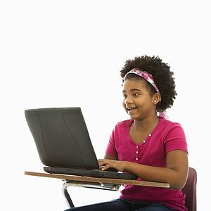 African American girl sitting in school desk typing on laptop computer.