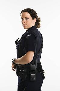 Portrait of mid adult Caucasian policewoman standing with hand on gun holster looking over shoulder at viewer.