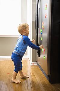 Caucasian toddler boy playing with magnets on refrigerator.