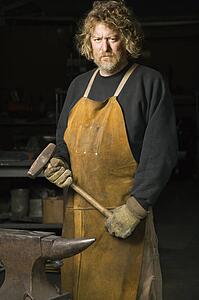 Metalsmith holding hammer with stern expression.
