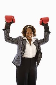 Businesswoman wearing boxing gloves holding arms up in victory stance and smiling