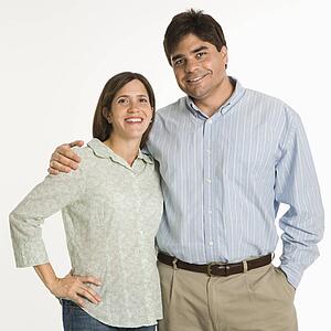 Couple standing smiling against white background.