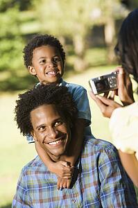 Father and son in park being photographed with digital camera.