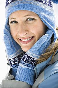 Portrait of attractive smiling mid adult woman wearing blue ski cap and gloves looking at viewer.