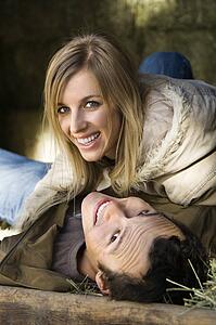 Couple lying in hay and smiling up at viewer