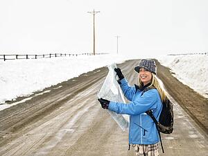 Woman in winter clothes standing on muddy dirt road holding open map smiling