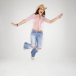 Young adult Caucasian woman wearing cowboy hat leaping into air with excited expression.