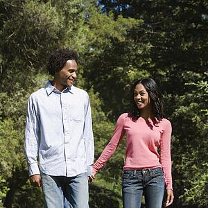 Smiling couple holding hands walking and talking in park.
