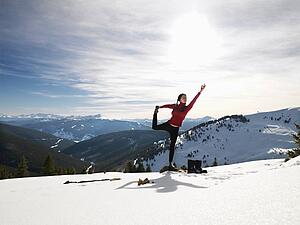 Woman doing yoga pose on rock in snow in mountainous terrain