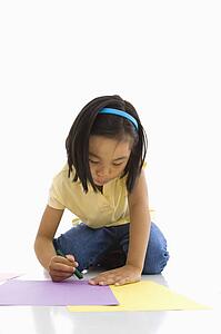 Asian girl sitting on floor coloring on paper.